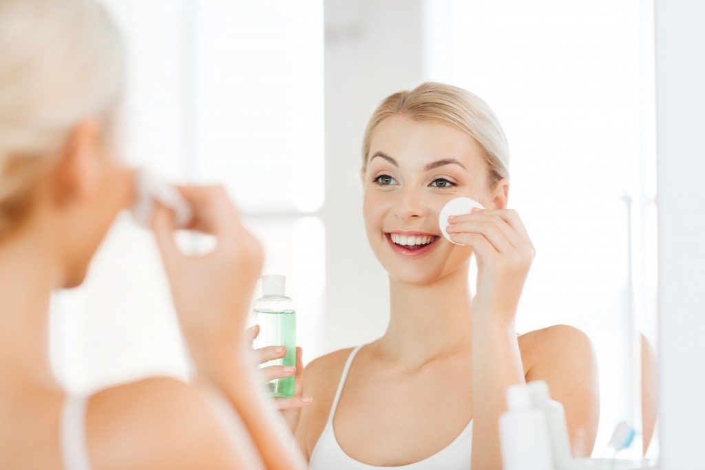 smiling young woman applying toner on her face