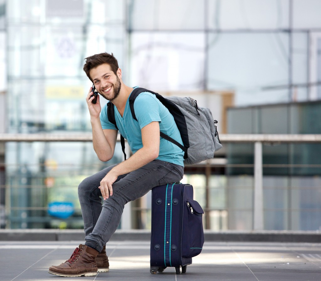 Man sitting on suitcase and calling by cellphone at airport