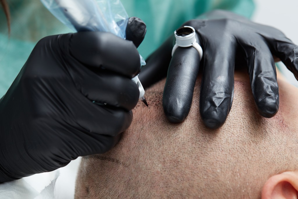 Cosmetologist making permanent makeup on man head