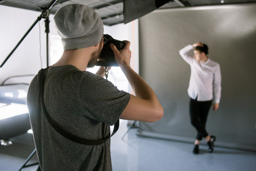 Photographer taking a shot of a model posing in a studio with a grey background.