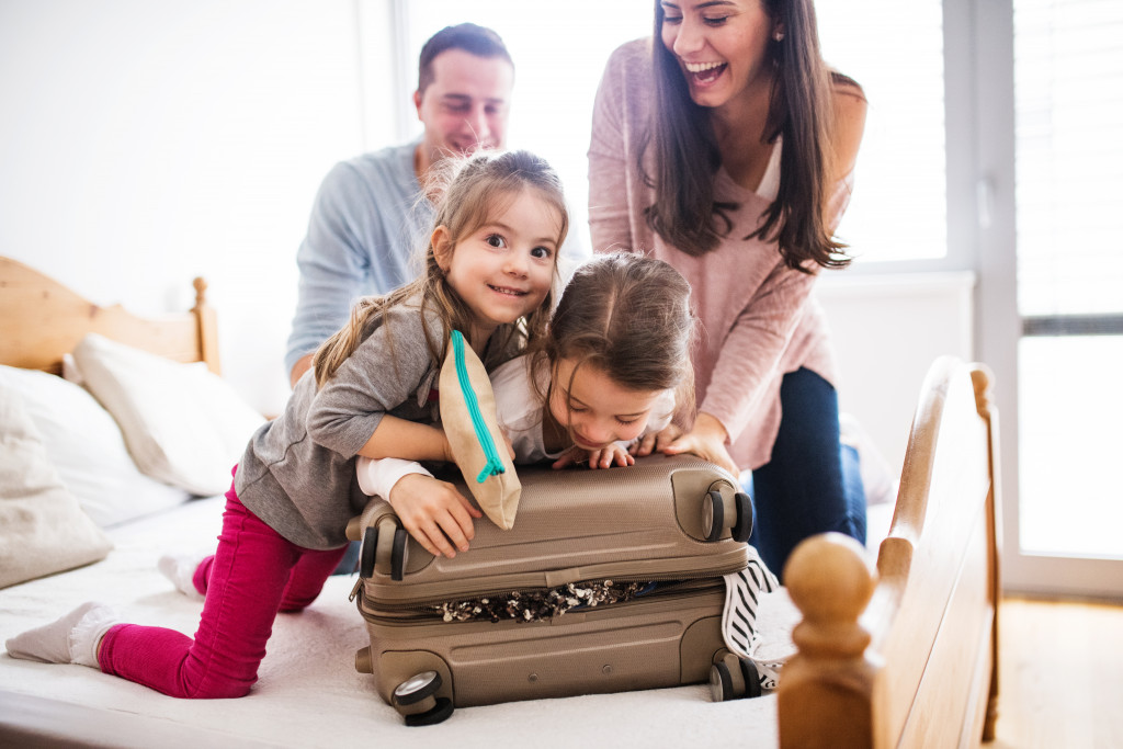 two young girls helping mother pack their luggage with father at the back