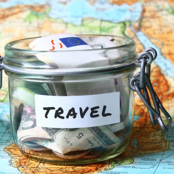 glass jar with money inside labeled travel on top of world map