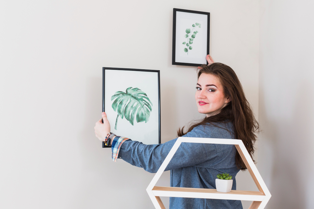 young woman fixing the picture frame on wall looking to camera